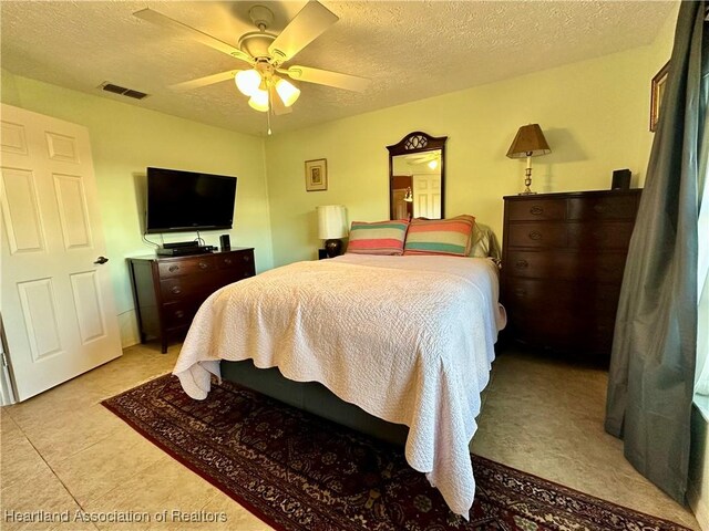 bedroom with light tile patterned floors, visible vents, a textured ceiling, and a ceiling fan