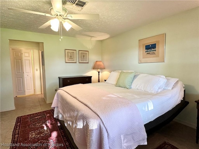bedroom featuring light tile patterned floors, a ceiling fan, baseboards, visible vents, and a textured ceiling