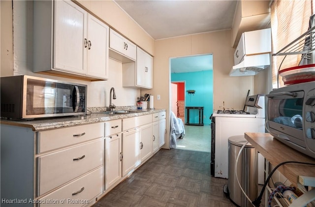 kitchen featuring stainless steel microwave, white cabinetry, a sink, gas range gas stove, and light stone countertops