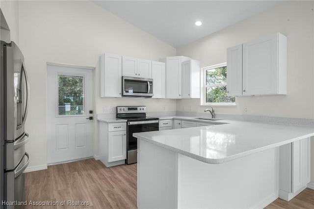 kitchen featuring kitchen peninsula, appliances with stainless steel finishes, vaulted ceiling, sink, and white cabinetry