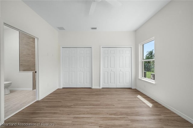 unfurnished bedroom featuring ceiling fan, light hardwood / wood-style floors, ensuite bathroom, and two closets