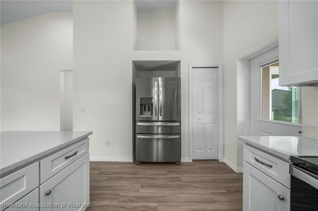 kitchen with light hardwood / wood-style flooring, stainless steel fridge with ice dispenser, range with electric stovetop, light stone countertops, and white cabinetry