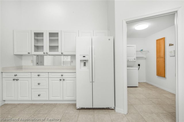 kitchen featuring white cabinets, white fridge with ice dispenser, and stacked washer / drying machine