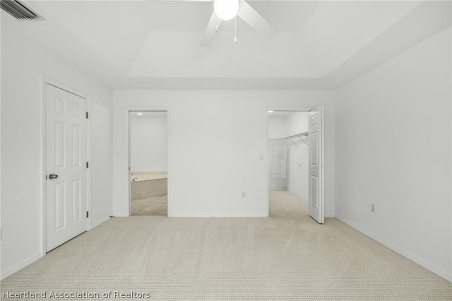 unfurnished bedroom with ensuite bathroom, light colored carpet, a tray ceiling, ceiling fan, and a spacious closet