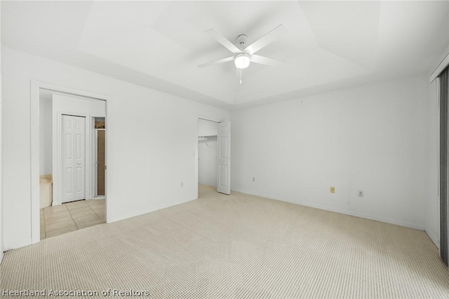 unfurnished bedroom featuring a tray ceiling, ceiling fan, and light colored carpet