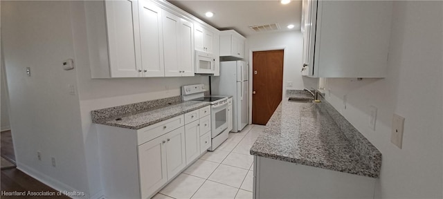 kitchen with white appliances, sink, light tile patterned flooring, light stone counters, and white cabinetry