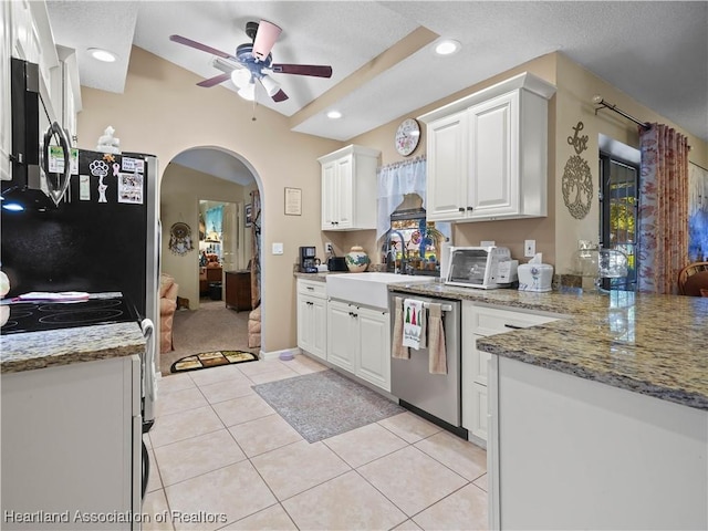 kitchen with light tile patterned floors, arched walkways, stainless steel appliances, white cabinetry, and a sink