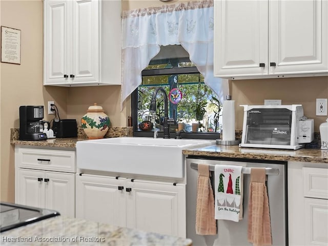 kitchen featuring dishwasher, dark stone countertops, a sink, and white cabinetry