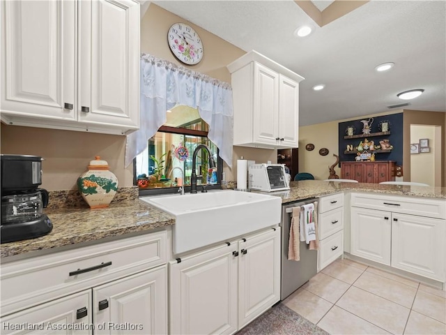 kitchen with light tile patterned floors, a peninsula, a sink, white cabinets, and dishwasher