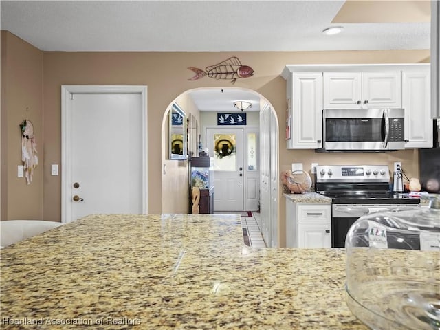 kitchen with stainless steel appliances, arched walkways, white cabinets, and light stone countertops