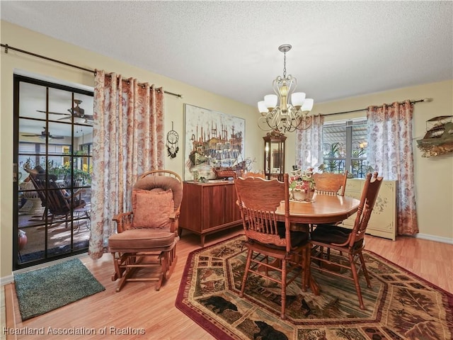 dining area featuring a textured ceiling, ceiling fan with notable chandelier, baseboards, and light wood-style floors