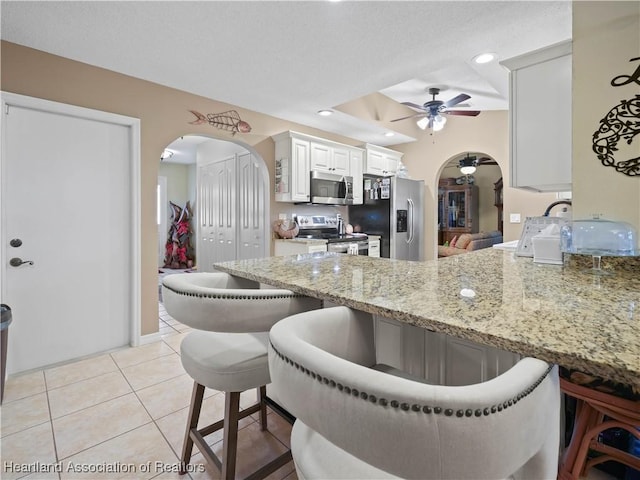 kitchen featuring arched walkways, appliances with stainless steel finishes, a breakfast bar area, white cabinetry, and light tile patterned flooring