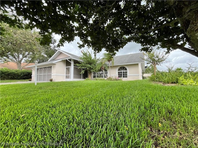 single story home with stucco siding, driveway, a front lawn, a sunroom, and a garage