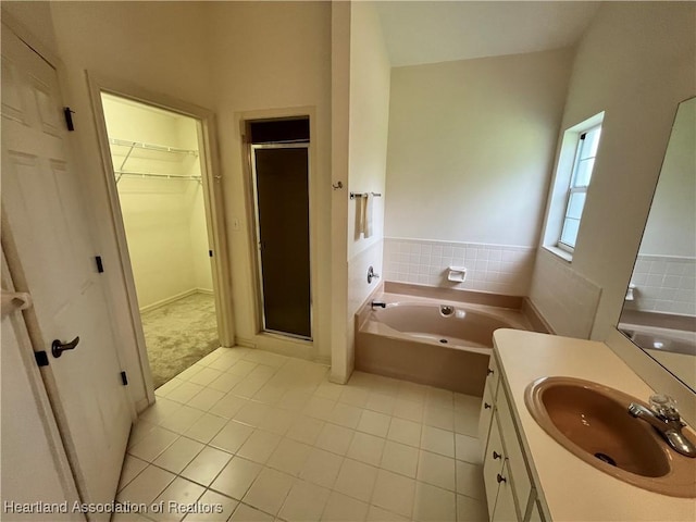 full bath featuring vanity, a shower stall, a walk in closet, a garden tub, and tile patterned floors