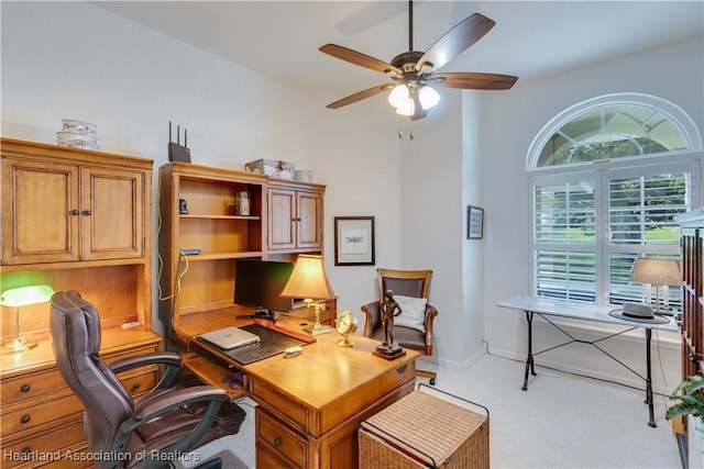 carpeted office space featuring a ceiling fan and baseboards