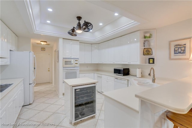 kitchen with wine cooler, a peninsula, white appliances, a sink, and a tray ceiling