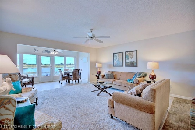 carpeted living room featuring a water view, ceiling fan, and a textured ceiling