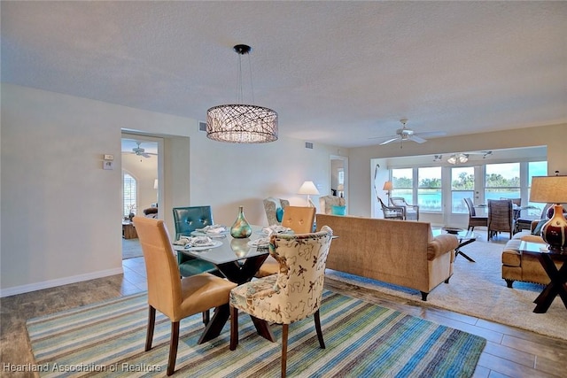 dining area with ceiling fan with notable chandelier and a textured ceiling