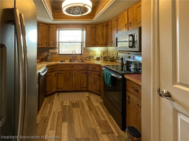 kitchen with stainless steel appliances, light wood-type flooring, a tray ceiling, and sink