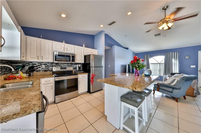 kitchen featuring stainless steel appliances, white cabinets, a sink, and light stone countertops