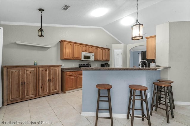 kitchen with visible vents, brown cabinetry, lofted ceiling, white microwave, and a breakfast bar