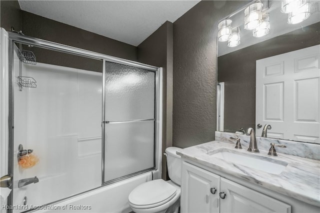 bathroom with toilet, enclosed tub / shower combo, vanity, and a textured wall