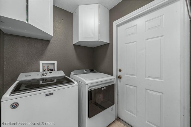 laundry area featuring a textured wall, washer and clothes dryer, and cabinet space