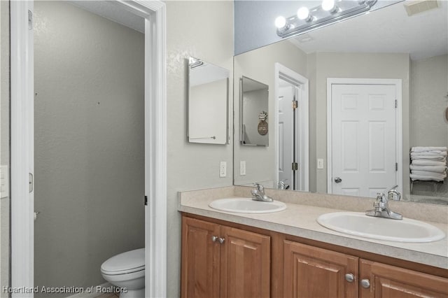 full bathroom with toilet, double vanity, a sink, and visible vents