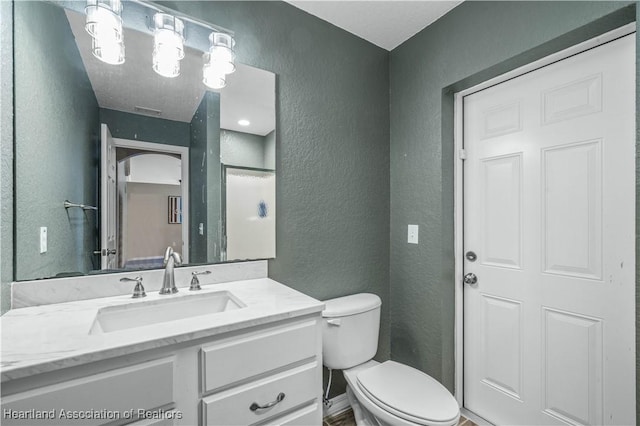 bathroom with visible vents, a textured wall, vanity, and toilet