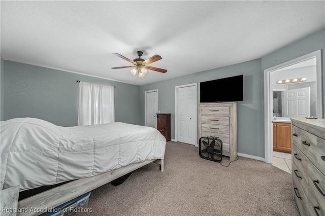 bedroom with light carpet, baseboards, ceiling fan, ensuite bathroom, and multiple closets