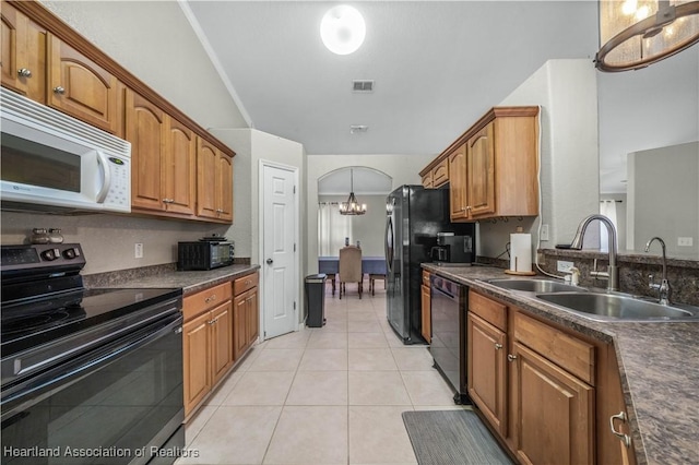 kitchen with arched walkways, dark countertops, brown cabinetry, a sink, and black appliances