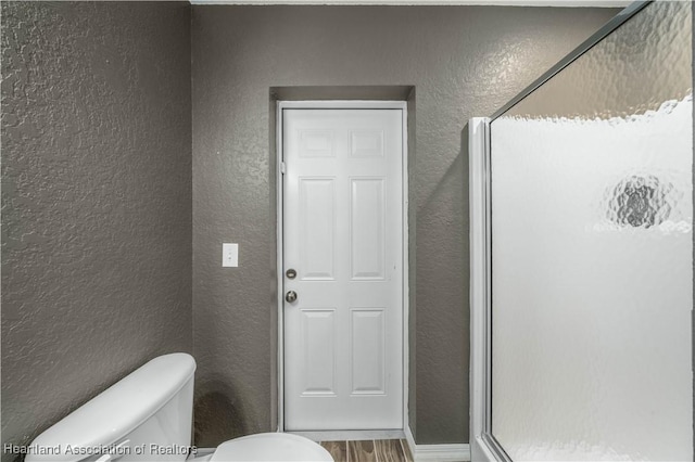 full bath featuring a textured wall, wood finished floors, a shower stall, and toilet