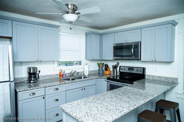 kitchen with light stone counters, a breakfast bar, stainless steel appliances, a sink, and a peninsula