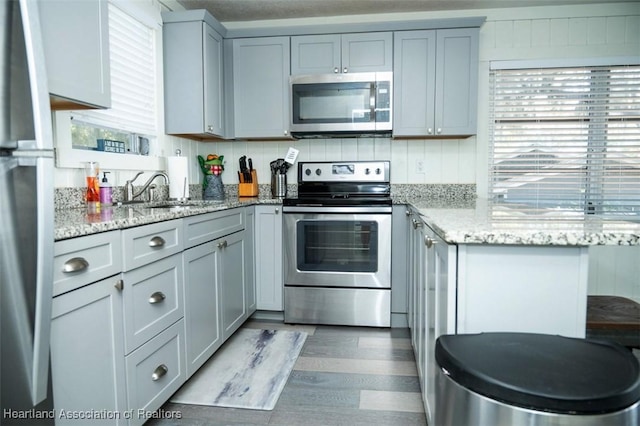 kitchen featuring appliances with stainless steel finishes, gray cabinets, a sink, and light stone countertops