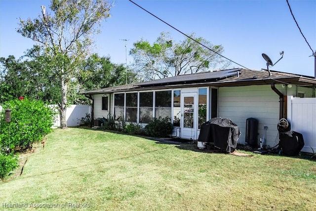 rear view of property featuring solar panels and a lawn