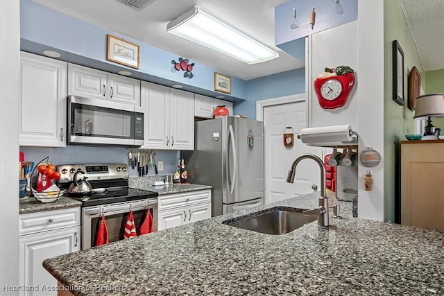 kitchen with stainless steel appliances, white cabinetry, dark stone counters, and sink