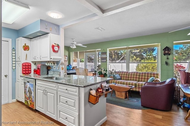 kitchen featuring dishwasher, white cabinets, sink, beamed ceiling, and light stone counters