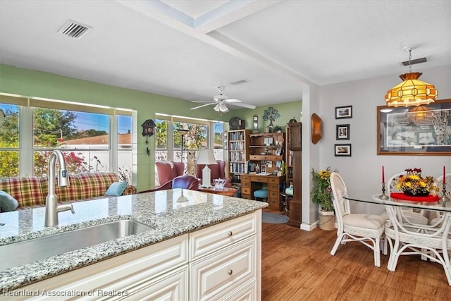 kitchen with light stone countertops, ceiling fan, sink, light hardwood / wood-style floors, and hanging light fixtures