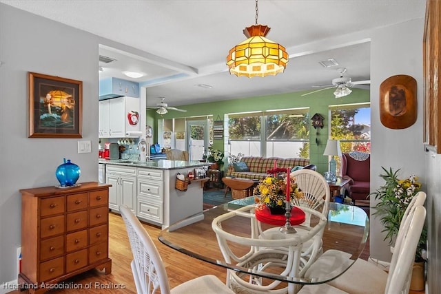 dining space featuring beam ceiling, light hardwood / wood-style floors, and sink