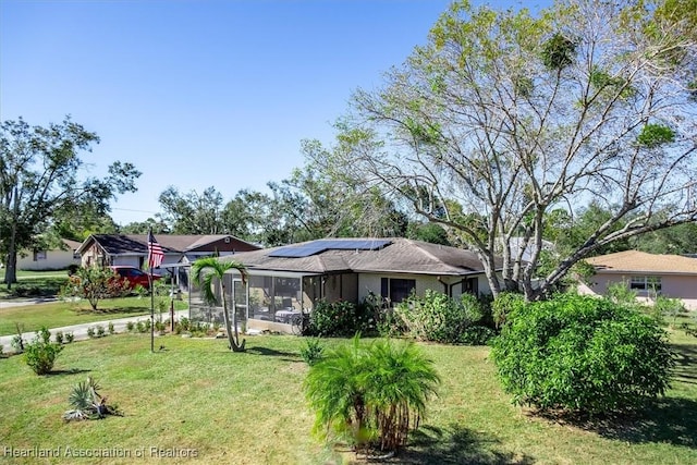 view of front of home with a sunroom, solar panels, and a front yard