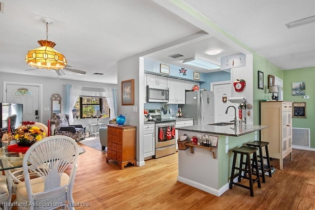 kitchen with appliances with stainless steel finishes, dark stone counters, a breakfast bar, sink, and white cabinetry