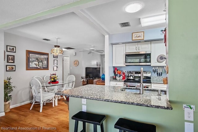 kitchen featuring kitchen peninsula, appliances with stainless steel finishes, decorative light fixtures, and white cabinetry