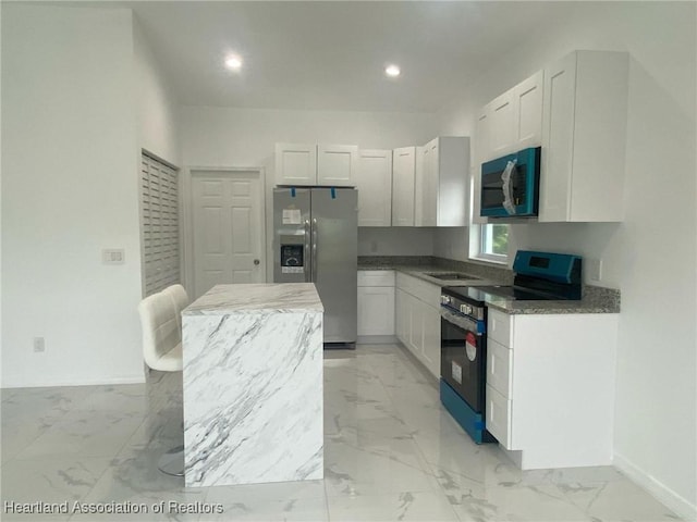 kitchen featuring white cabinets, a center island, stainless steel appliances, and dark stone counters