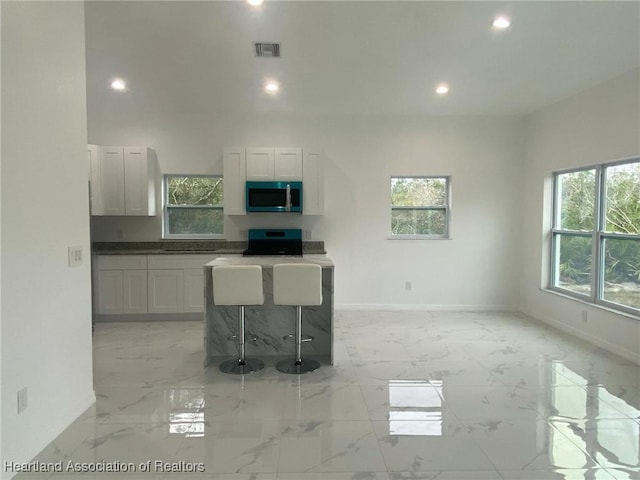 kitchen featuring a kitchen bar, white cabinetry, and range with electric stovetop