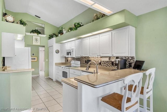 kitchen with sink, white appliances, white cabinetry, vaulted ceiling, and kitchen peninsula