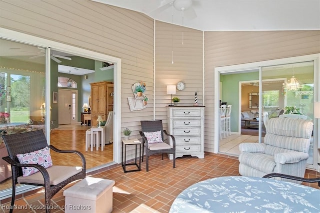 living room with ceiling fan, lofted ceiling, and wooden walls