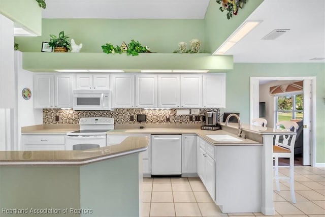 kitchen with sink, white cabinets, light tile patterned floors, kitchen peninsula, and white appliances