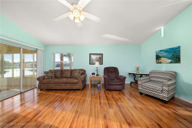 living area with vaulted ceiling, a water view, light wood finished floors, and a ceiling fan