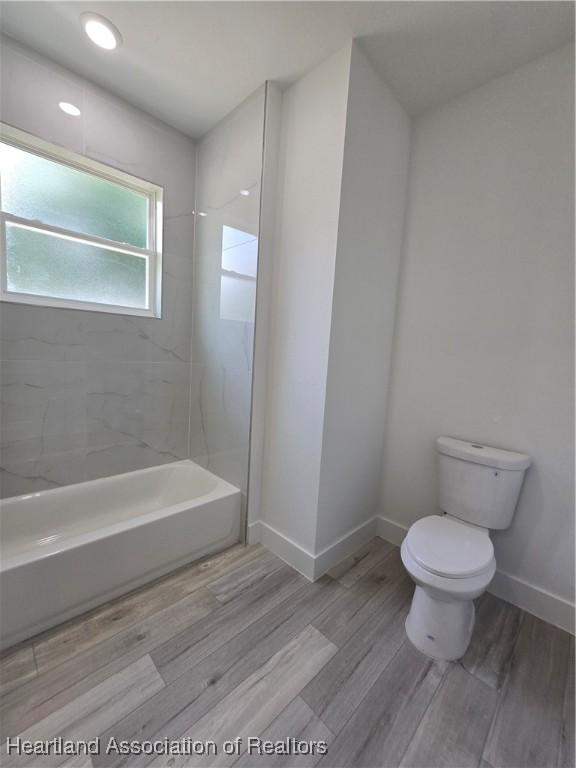 bathroom featuring tiled shower / bath combo, toilet, and wood-type flooring