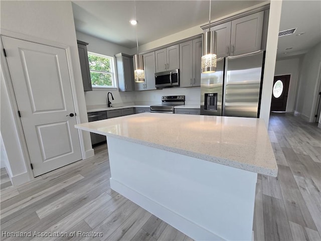 kitchen with light stone countertops, appliances with stainless steel finishes, sink, a kitchen island, and hanging light fixtures